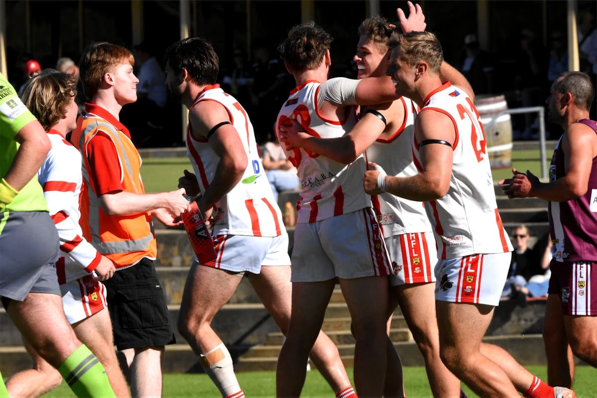 Australian rules football players in red and white guernseys celebrating together on the oval