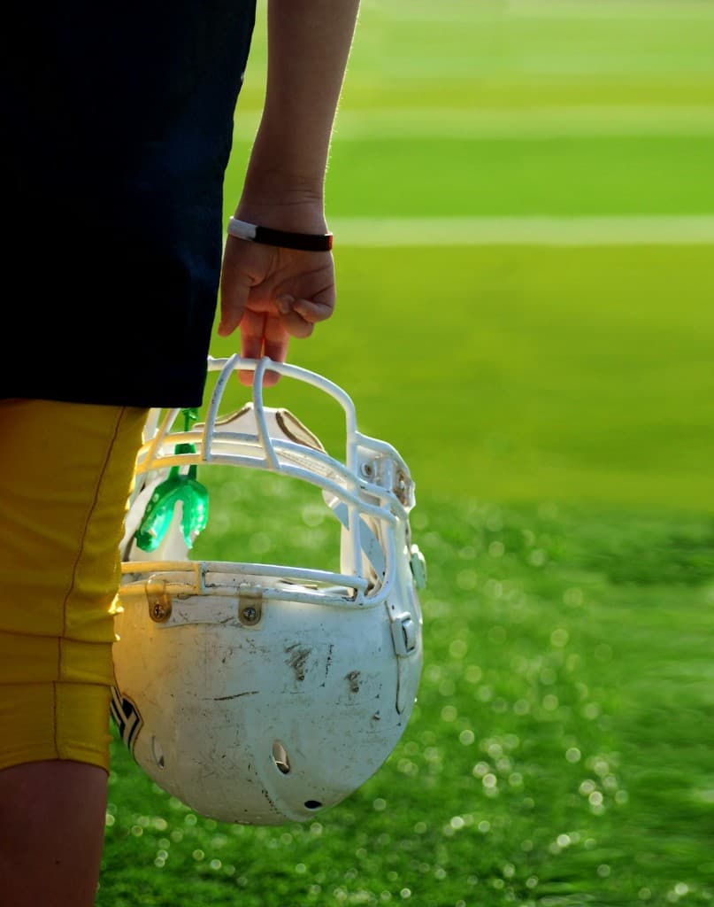 Football player holding a helmet on the field — concussion and brain health awareness