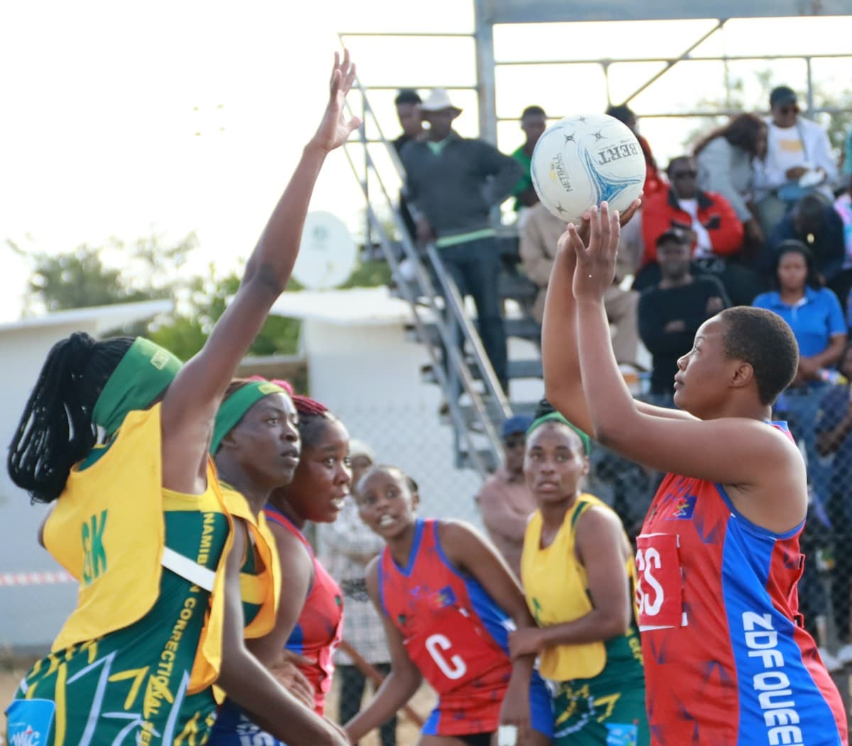 Netball goal shooter and goal keeper contesting a shot on an outdoor netball court